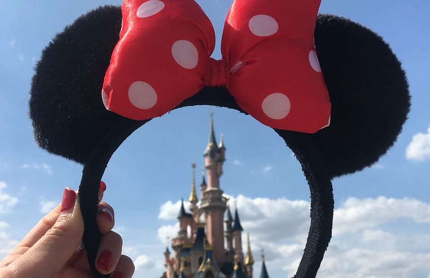 person holding Minnie Mouse headband overlooking castle